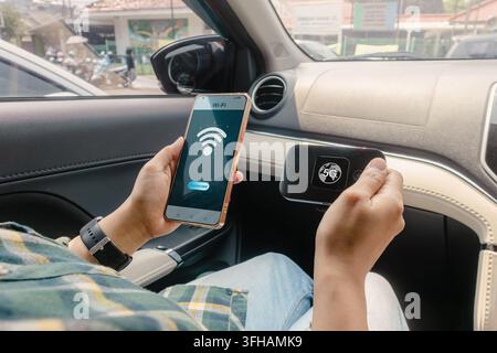 Une personne assise dans une voiture tenant un dispositif de point d'accès Wi-Fi portable 5G et un smartphone. Connexion du smartphone au point d'accès mobile. Banque D'Images