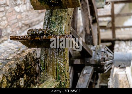 Vue rapprochée d'une ancienne roue à eau en bois avec du bois mouillé, de la mousse et des gouttes d'eau à côté d'un mur de pierre, montrant une construction mécanique traditionnelle et Banque D'Images