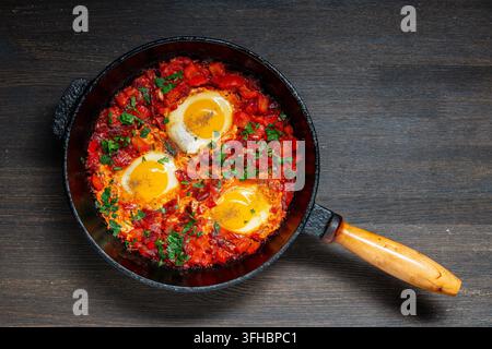 Shakshuka dans une poêle en fonte, vue de dessus, gros plan. Shakshuka traditionnelle du Moyen-Orient avec trois œufs frits pochés dans une sauce tomate et poivron épicée Banque D'Images