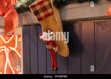 Chaussette de Noël rustique en toile de jute avec une poupée du Père Noël joyeuse, suspendue à une cheminée en bois ornée d'une guirlande festive, évoquant un esprit de Noël chaleureux Banque D'Images