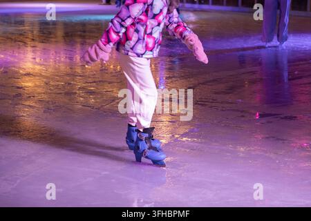 gros plan des jambes d'une personne et de patins bleus glissant sur une surface de glace brillamment éclairée, symbolisant une activité récréative hivernale, un plaisir festif en plein air Banque D'Images
