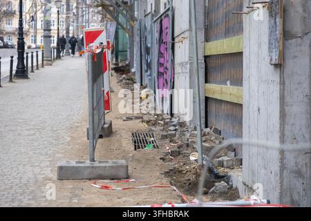 Une vue détaillée d'une zone de construction urbaine avec une barrière rouge et blanche le long d'un trottoir pavé de la ville, illustrant le progrès dans l'entretien des infrastructures Banque D'Images
