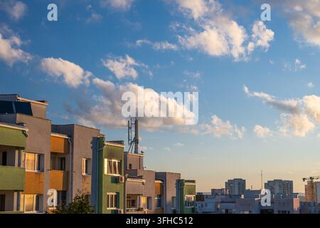 Les toits d'immeubles résidentiels modernes et les antennes de télécommunication se dressent contre un ciel bleu rempli de nuages d'après-midi baignés de soleil. Banque D'Images