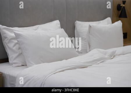 Des oreillers blancs reposent sur un lit fait avec des draps propres dans une chambre contemporaine, mettant l'accent sur un design minimaliste et un repos paisible pour des projets de design d'intérieur Banque D'Images
