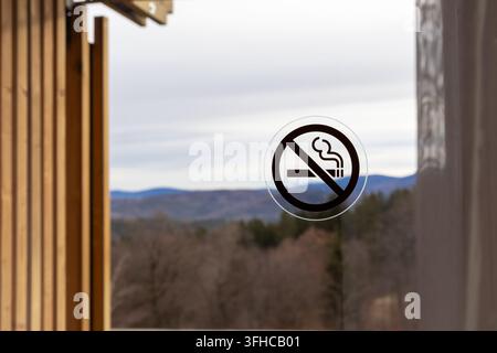 Vue rapprochée d'un autocollant de signalisation « non-fumer » bien visible sur une vitre, avec un paysage naturel serein et flou visible à l'extérieur, renforçant le calme Banque D'Images