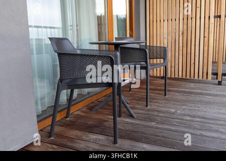 Un balcon confortable doté de chaises noires modernes et d'une table ronde, installé sur une terrasse en bois patiné parfaite pour une zone de détente extérieure tranquille Banque D'Images