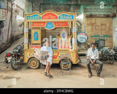 Deux hommes assis à côté d'un chariot Azaad Band décoré de couleurs vives dans une rue de Bundi, Rajasthan, Inde, l'un des hommes lisant un journal Banque D'Images