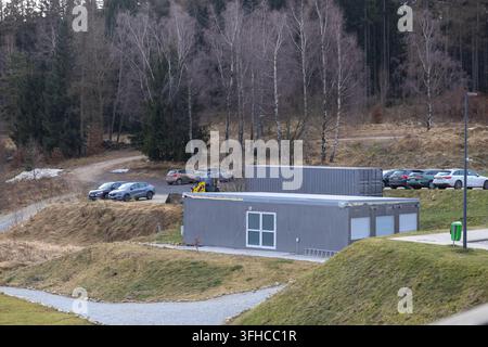 Szklarska Poręba, Pologne – 16 décembre 2025 : des bâtiments modulaires en conteneurs gris et des véhicules garés sur une route de gravier se trouvent dans un paysage vallonné sec Banque D'Images