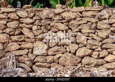 Grossissement horizontal d'un mur de pierre sec traditionnel fait de roches brunes naturelles à Alanya, Turquie. Des feuilles de bananier vertes et luxuriantes sont visibles au-dessus Banque D'Images