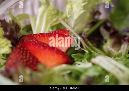 Une photographie macro détaillée capturant des tranches de fraises rouges vives et mûres reposant sur un lit de salade verte mélangée. Banque D'Images
