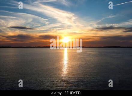 Le soleil plonge sous l'horizon, peignant le ciel de couleurs chaudes et se reflétant sur la surface paisible de l'eau Banque D'Images