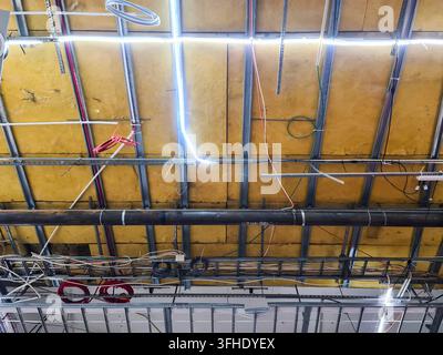Plafond industriel exposé révélant l'isolation, le cadre métallique, les câbles électriques et divers tuyaux utilitaires Banque D'Images