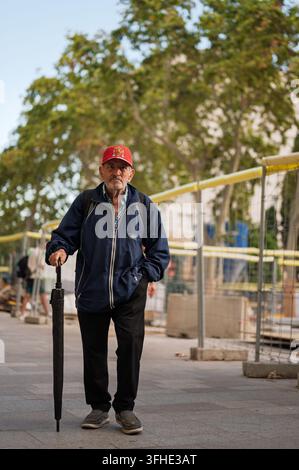 Un homme âgé portant une casquette plate et tenant une canne passe devant des travaux de construction sur La Rambla à Barcelone, en Espagne. Banque D'Images