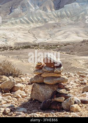 Un cairn rustique construit à partir de calcaire pâle et de pierres couleur rouille se dresse sur une crête désertique rocheuse surplombant un paysage de canyon brumeux. Banque D'Images
