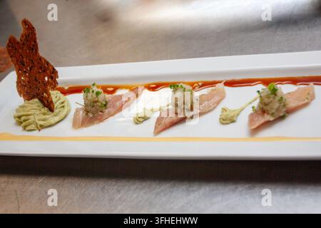 Une entrée de crudo de poisson finement arrangée sur une assiette rectangulaire allongée, mettant en vedette du poisson blanc cru finement tranché, recouvert d'un mi Banque D'Images