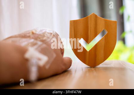 Concept d'assurance maladie et de protection médicale, main de patient avec cathéter IV reposant sur une table à côté d'un bouclier en bois avec une coche, symbolisant Banque D'Images
