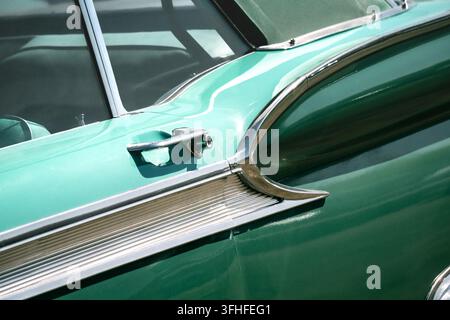 Close-up d'une automobile Cadillac vintage turquoise montrant son capot sculpté, sa moulure latérale chromée, son ornement de capot, sa poignée de porte et son pare-brise sous une lumière vive Banque D'Images