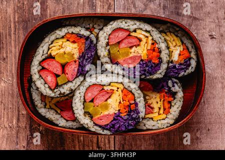 Kimbap (ou gimbap) coloré avec des légumes et de la saucisse dans une boîte en bois sur une surface en bois Banque D'Images