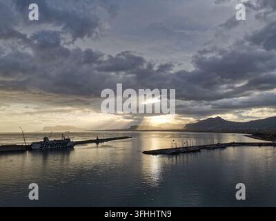 PALERMO, ITALIE - 12 JANVIER 2023 : Une ferri Siremar est amarrée dans le port de Palerme alors que des rayons de soleil traversent des nuages dramatiques sur la côte sicilienne à l'aube Banque D'Images