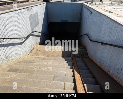 Des escaliers en pierre avec des rails de guidage en métal descendent dans un passage souterrain sous une rue urbaine animée, démontrant une infrastructure de transit urbain essentielle Banque D'Images