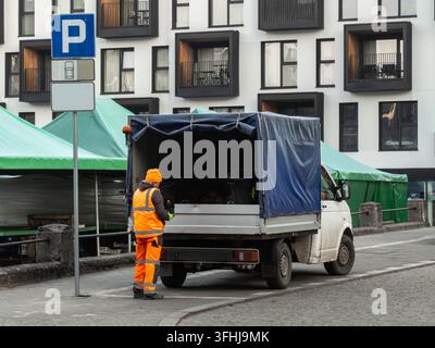 Un opérateur portant un équipement de sécurité vif organise le matériel à l'arrière d'un pick-up recouvert d'une bâche, mettant en évidence une logistique efficace de la chaîne d'approvisionnement Banque D'Images