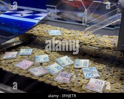 Machine de poussée de pièces d'arcade empilée avec des piles de jetons dorés et des billets enfermés, représentant un environnement de divertissement interactif concentré Banque D'Images