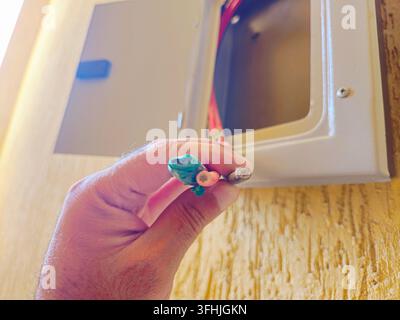 Sud-Sinaï, Égypte, 30 août 2026 : un tableau électrique ouvert avec une main tenant trois fils électriques isolés exposés de couleur verte (scotchés), r Banque D'Images