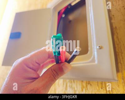 Sud-Sinaï, Égypte, 30 août 2026 : un tableau électrique ouvert avec une main tenant trois fils électriques isolés exposés de couleur verte (scotchés), r Banque D'Images
