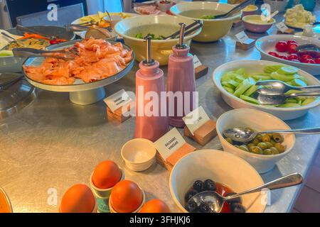Différents plats sont disposés sur des tables dans une salle à manger. Il y a des tranches de saumon, des légumes frais, des œufs et des bols d'olives. Les invités peuvent choisir fro Banque D'Images