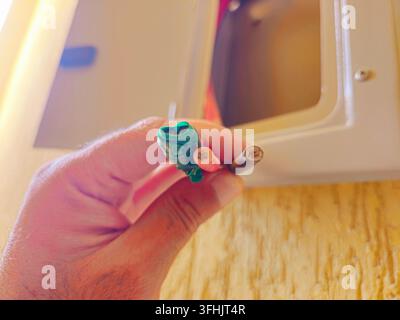 Sud-Sinaï, Égypte, 30 août 2026 : un tableau électrique ouvert avec une main tenant trois fils électriques isolés exposés de couleur verte (scotchés), r Banque D'Images