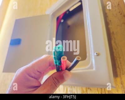 Sud-Sinaï, Égypte, 30 août 2026 : un tableau électrique ouvert avec une main tenant trois fils électriques isolés exposés de couleur verte (scotchés), r Banque D'Images