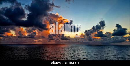 Nuages imposants illuminés par la lumière chaude du lever du soleil sur la mer calme et ouverte Banque D'Images