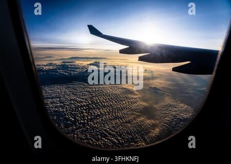 Vue aérienne époustouflante depuis la fenêtre de l'avion au coucher du soleil montrant l'aile et un vaste paysage nuageux en dessous Banque D'Images