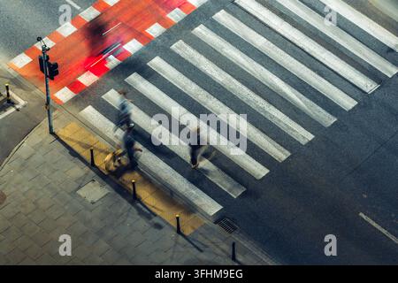 Vue aérienne de personnes traversant un passage piéton avec flou de mouvement et une piste cyclable rouge dans un cadre urbain en Pologne. Banque D'Images