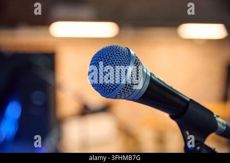 Micro en maille bleue s'étendant à travers un studio d'enregistrement chaleureux avec des lumières floues, un équipement sombre et une mise au point peu profonde, offrant une imagerie audio claire pour Broa Banque D'Images