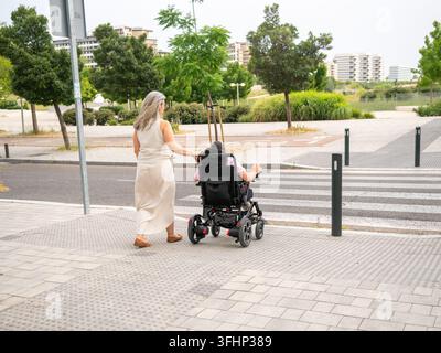 Aide-soignante assistant une femme âgée dans un fauteuil roulant électrique à utiliser un passage piéton Banque D'Images
