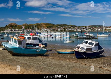 Bateaux de pêche reposant sur un rivage de boue et de gravier à marée basse dans le port de Conwy, dans le nord du Pays de Galles, avec les collines de l'estuaire et les bâtiments de la ville de l'autre côté de l'eau ouverte Banque D'Images