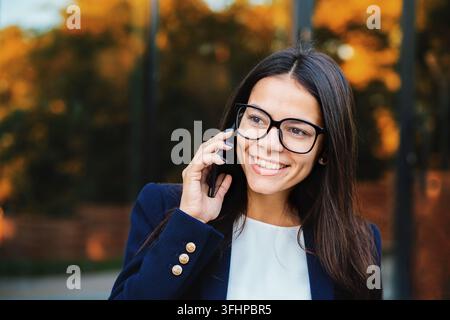 Businesswoman ont conversation à l'aide de téléphone mobile. Fille d'affaires formel dans les verres et les adapter à des pourparlers avec la joie d'un collègue. Le travail au salaire de l'employé de bureau, Banque D'Images