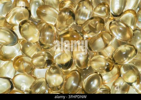 Une vue macro par le dessus d'un tas dense de gélules softgel translucides jaune doré. La surface en gélatine brillante reflète une lumière chaude, créant des reflets brillants hi Banque D'Images