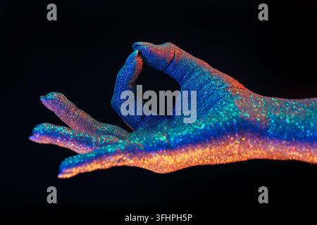 Jnana Gian mudra - Om sur fond noir.Femme à la main recouverte de paillettes holographiques brillantes sous couleur néon Banque D'Images