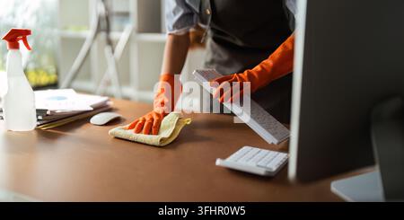 Femme asiatique nettoyant dans une pièce de travail à la maison. Jeune femme de ménage utilise un chiffon pour essuyer l'équipement de travail. concept ho Banque D'Images