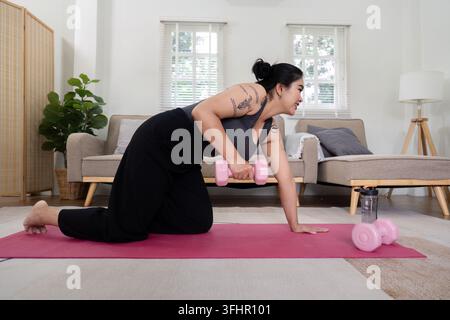 Femme en surpoids déterminée faisant de l'exercice à la maison avec des haltères, engagée dans son parcours de perte de poids et de fitness, démontrant Stren Banque D'Images