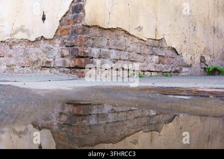 Mur de briques avec une fissure dedans et une flaque d'eau reflétant le mur. Le reflet du mur est déformé et flou, donnant l'impression de Banque D'Images