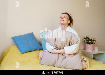 Une femme est assise sur un lit avec un oreiller sur la tête Banque D'Images