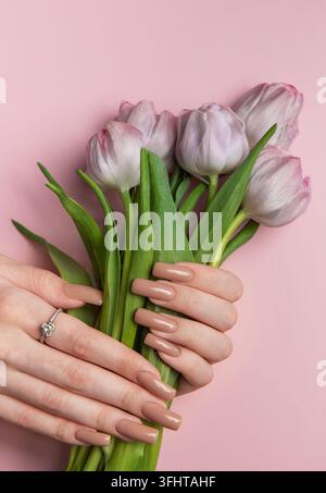 Mains de femme avec une manucure parfaite tenant un magnifique bouquet de tulipes violettes sur fond rose Banque D'Images