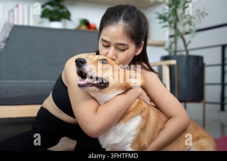 Moment affectueux. Femme embrassant son chien corgi dans un cadre intérieur confortable. Banque D'Images