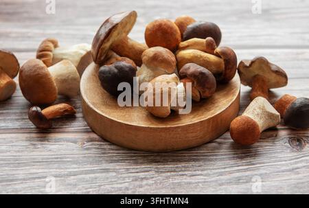 Différents types de champignons sauvages sur une assiette en bois exposée sur une table en bois rustique à la lumière naturelle Banque D'Images