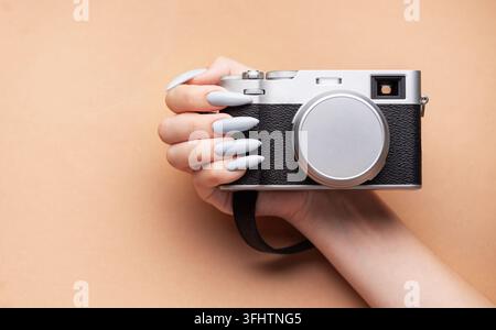 Main de femme avec un vernis à ongles gris tenant un appareil photo Banque D'Images