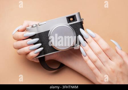 Main de femme avec un vernis à ongles gris tenant un appareil photo Banque D'Images