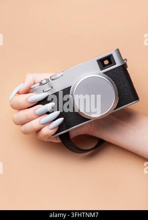 Main de femme avec un vernis à ongles gris tenant un appareil photo Banque D'Images